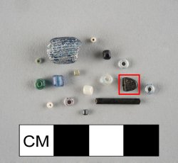 Black, ovular, unidentified object with possible double perforation, flat sides.