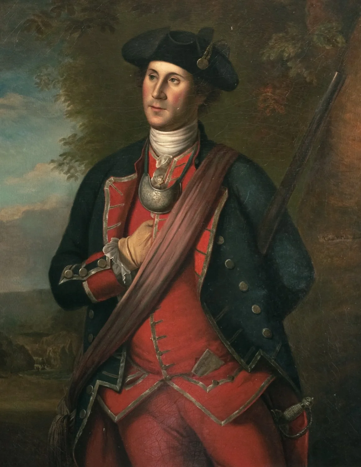 A young man wearing a a blue and red coat. Left hand is coving his heart under a red sash