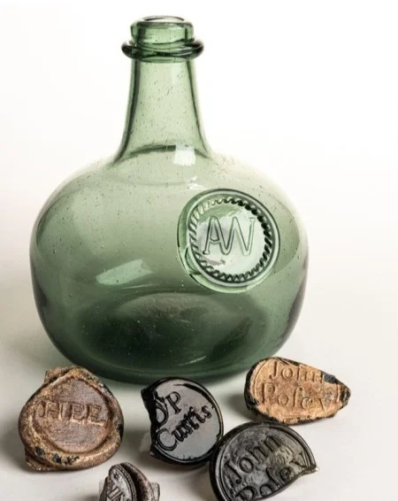 A reproduction wine bottle with Augustine Washington’s seal alongside the wine bottle seals excavated on Mount Vernon property to date. (MVLA)