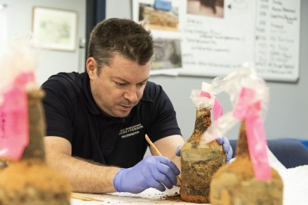 Mount Vernon Principal Archaeologist Jason Boroughs removes soil from one of the 35 glass bottles discovered in Washington's cellar. (MVLA)