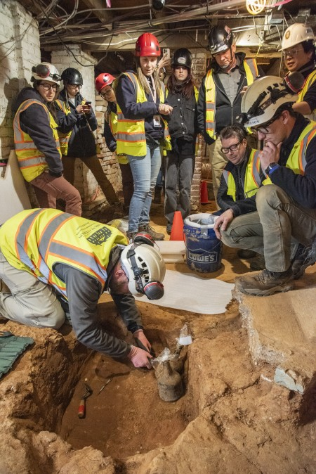 Mount Vernon’s Archaeology team watches with anticipation as project archaeologist Nick Beard removes the first bottle from the ground. (MVLA)