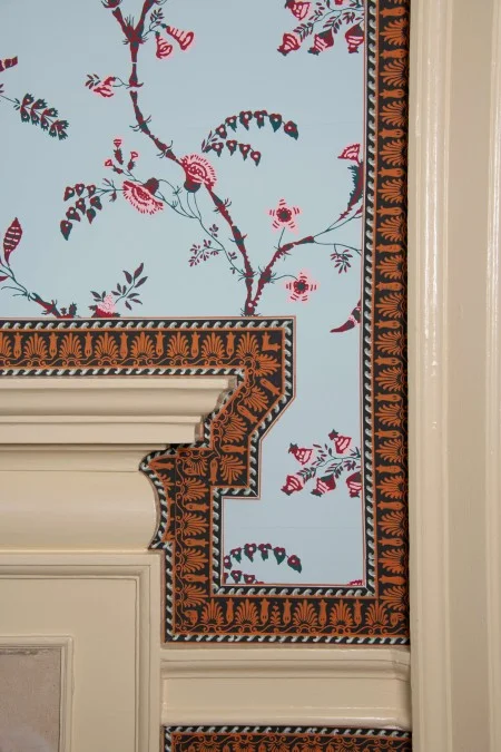 View of the wallpaper and border alongside the cream-colored paint on the mantel and door architrave.