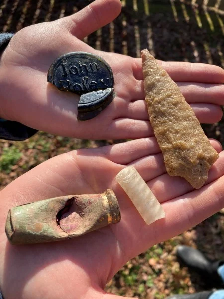 A collection of artifacts from the North Grove, including an almost complete John Posey wine bottle seal, a projectile point with a stemmed base, an enamel twist wine glass stem, and a mid-20th-century lipstick tube which seems to have been hit with a tent spike or something similar. (MVLA)