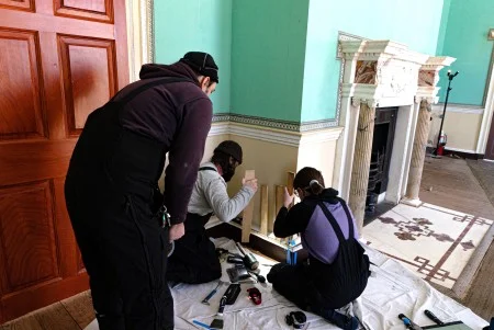 Assistant Restoration Manager Steve Fancsali (standing) and Preservation Carpenter Joe Zemp (left) and Preservation Carpenter Allison Brashears use wedges to work apart the different components of the room’s mopboards. (MVLA)